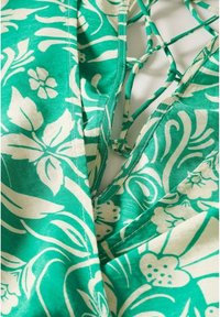 Tissu à motif floral vert et blanc avec des détails de liens croisés sur un décolleté.
