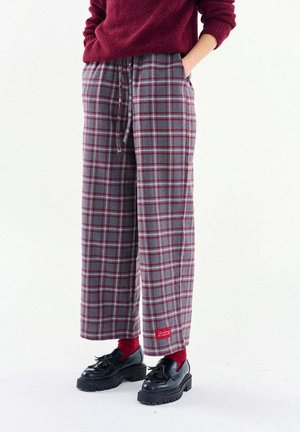 Osoba ubrana w szerokie spodnie w szaro-czerwoną kratę z troczkiem, czerwone skarpetki, czarne mokasyny z frędzlami oraz czerwony sweter z podwiniętymi rękawami.