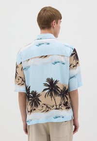 Camisa de manga corta azul con estampado de palmera y paisaje. El material parece ligero y suave, con un ajuste relajado.