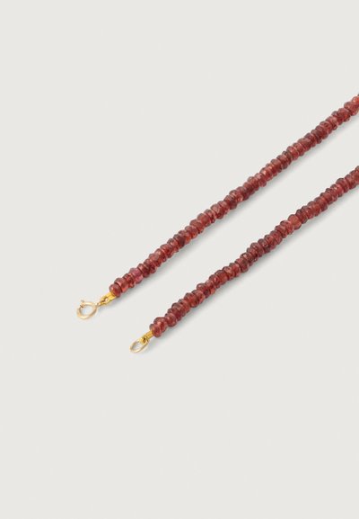 Raudona karoliukų apyrankė su mažais, tekstūruotais karoliukais, užsegta auksinės spalvos užsegimais abiejuose galuose. Karoliukai yra netaisyklingos formos ir arti vienas kito.