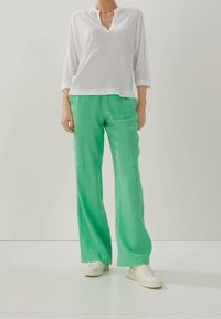 Vitt långärmad topp med v-ringning. Gröna vida linbyxor. Modellen har på sig vita sneakers. Slät textur, avslappnad passform.