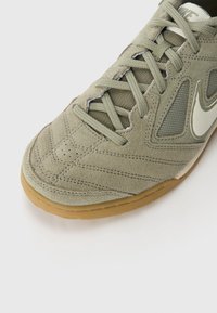 Light green suede sneaker with mesh panels, a textured toe, and a rubber gum sole. Features signature checkmark logo in white.