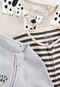 Three baby outfits: one beige with black spots, one grey with a front snap, and one pink striped. All feature soft cotton fabric.