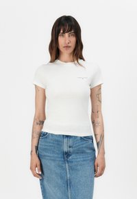 Vit bomull t-shirt med korta ärmar och rund halsringning, med en liten svart logotyp på vänster bröst och figurnära silhuett.