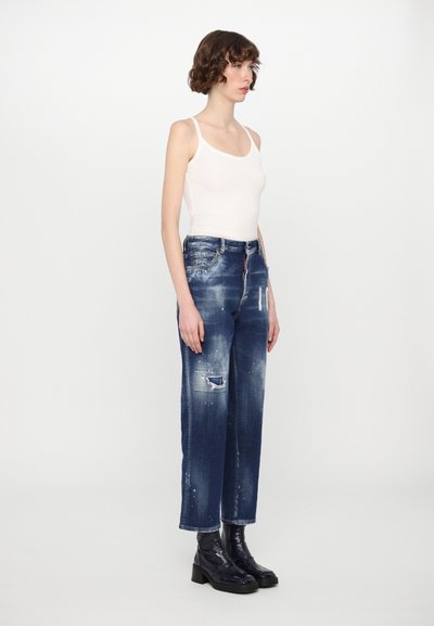 Jeans in denim blu scuro a vita alta con una vestibilità ampia, aree sbiadite, orlo sfilacciato e dettagli di spruzzi di vernice bianca. Abbinati a stivaletti neri.