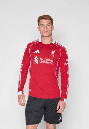 Rode longsleeve voetbaltop met witte accenten en branding. Beschikt over een textiel met structuur, ronde hals en logo's op de borst en mouwen.