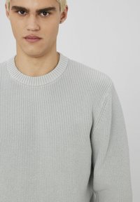 Pull en maille gris clair avec une texture côtelée et un col rond. Le tissu a l'air doux et décontracté avec des manches longues.