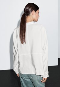 Hvid sweatshirt med en løs pasform, rund halsudskæring og lange ærmer. Den har en sømdetalje ned ad ryggen og er kombineret med lyseblå denim.