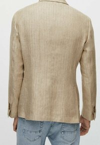 Beżowa lniana marynarka o dopasowanym kroju, z dwoma guzikami na mankietach, rozcięciem z tyłu oraz gładką fakturą, zestawiona z jasnoniebieskimi dżinsami.