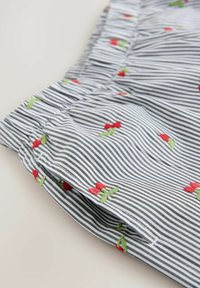Gros plan sur un tissu rayé noir et blanc orné de petites fleurs rouges brodées et de feuilles vertes, avec un détail élastique froncé.