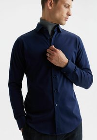 Granatowa koszula z długim rękawem zapinana na guziki, o gładkiej fakturze i subtelnym połysku, z klasycznym kołnierzykiem i dopasowanym krojem.