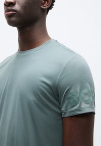 Πράσινο πλεκτό αθλητικό πουκάμισο με κοντά μανίκια. Το υφασμένο ύφασμα διαθέτει ορατό μοτίβο πλέγματος. Τοποθετημένο διακριτικά το "BOK" στο μανίκι.