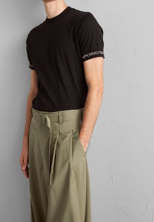T-shirt en coton noir avec encolure ronde côtelée et logo "EMPORIO ARMANI" brodé sur les manches, assorti à un pantalon plissé vert olive.