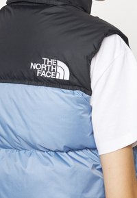 Czarna i jasnoniebieska puchowa kamizelka z wysokim kołnierzem, z haftowanym białym logo "THE NORTH FACE" na górnej części pleców.