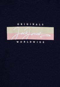 Jūras zila kokvilnas T-krekls ar horizontālu grafiku, kurā ir krēmkrāsas, rozā un baltas krāsas teksta uzraksti "Jack Jones" un "Originals Worldwide."