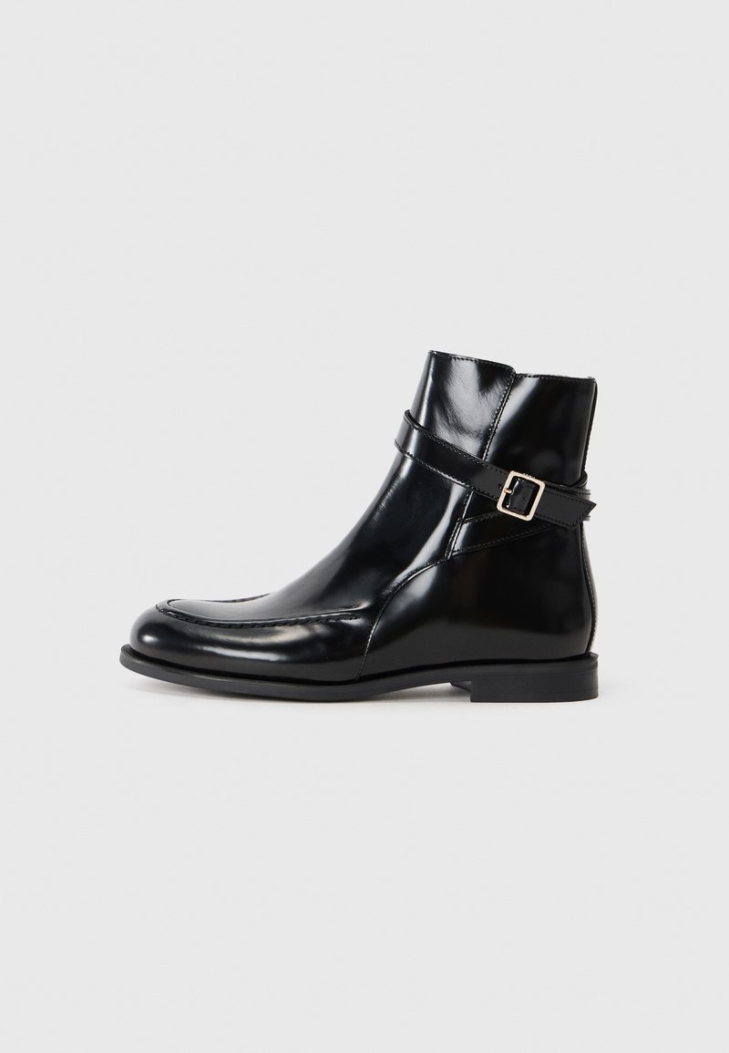 Botas de tornozelo em couro preto com um acabamento brilhante, apresentando uma faixa decorativa e fivela, bico arredondado e um salto baixo empilhado.