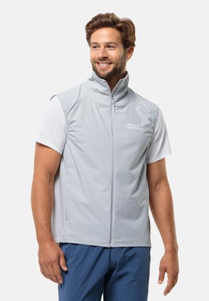 Grijze mouwloze jas gemaakt van lichtgewicht, ademend materiaal. Heeft een hoge kraag en een rits aan de voorkant, gecombineerd met een wit T-shirt met korte mouwen.