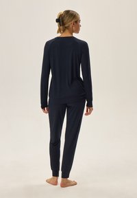 Granatowy zestaw loungewear składający się z długiego rękawa bluzki z okrągłym dekoltem oraz dopasowanych spodni zwężających się ku dołowi z elastycznymi mankietami, wykonany z miękkiej tkaniny.