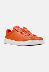 Sneakers in pelle arancione con suole in gomma bianca, caratterizzati da accenti in tessuto rosso e lacci a contrasto, progettati con una forma elegante e minimal.