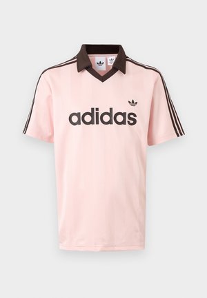 Camiseta rosa claro de Adidas de manga corta con cuello marrón oscuro, rayas en los hombros y un gran logo de Adidas en el frente.