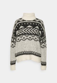 Stickad tröja i krämfärg med svarta geometriska mönster. Har en hög polokrage, ribbade ärmslut och en lös passform. Texturen ser mjuk och varm ut.