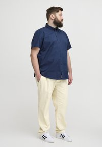 Marineblå kortermet skjorte med knapper, løse kremfargede bukser og hvite joggesko med svarte striper. Enkelt design, bomullsstoff, avslappet passform.