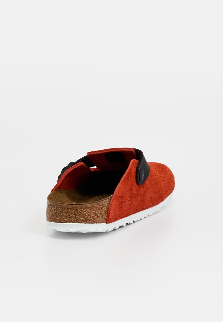 Rote Wildleder-Slipper mit einem schwarzen Akzentriemen, Korkfußbett und weißer Gummisohle. Hat eine abgerundete Rückseite und ein minimalistisches Design.