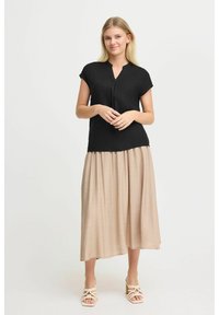Top nero a maniche corte con scollatura a V, abbinato a una gonna fluida beige. Tessuto leggero con drappeggio morbido. Sandali bianchi open-toe.