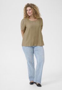 Haut vert olive à manches courtes avec un col arrondi, associé à un jean évasé bleu clair. Des chaussures noires plates complètent la tenue.