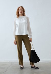 Bílá blůza s nafouknutými rukávy, olivově zelené kalhoty na míru, černá suede kabelka s řetízkem a tmavé baleríny.