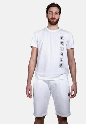 T-shirt bianca in cotone con scritta "COLMAR" in nero sul lato sinistro, abbinata a pantaloncini bianchi con logo circolare sull'orlo.
