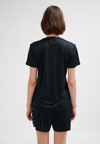 Czarny sportowy t-shirt z krótkimi rękawami, gładką fakturą, luźnym krojem i detalami na tylnej części ramion. W połączeniu z czarnymi szortami.