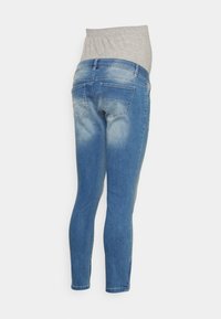 Calças de maternidade em denim azul com um cós elástico cinza, apresentando um design slim fit e detalhes nos bolsos traseiros. Efeito de lavagem desbotada.