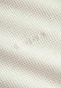 Baltas tekstūruotas audinys su vaflinio tipo raštu. Pabrėžiamas subtilus "GABBA" siuvinėjimas suderinta siūlų spalva.