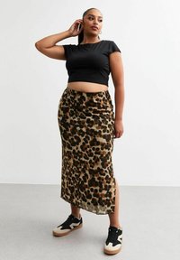 T-shirt noir court, jupe en satin à imprimé animal avec des taches vertes et brunes, fente sur le côté, associée à des baskets noires et beiges.