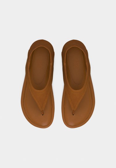 Ζευγάρι καφέ δερμάτινα σανδάλια τύπου flip-flop με φαρδιές λουρίδες και στρογγυλεμένο σχεδιασμό μύτης, τοποθετημένα επίπεδα σε ανοιχτό φόντο.