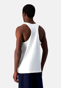 Hvid bomulds tanktop med racerback-design, der har en glat tekstur og en afslappet pasform, båret sammen med mørkeblå shorts.