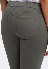 Jeans de mezclilla elástica gris con una silueta ajustada, que cuentan con dos bolsillos traseros y una cintura alta. Tejido texturizado con detalles de costura visibles.