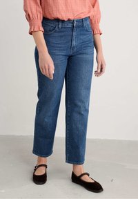 Hoge taille blauwe denim jeans met een rechte snit, vervaagde textuur en vijf zakken. Gecombineerd met zwarte platte schoenen en een roze blouse.