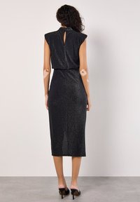 Vestido midi negro sin mangas hecho de un tejido brillante. Presenta un cuello alto y detalle de abertura en la parte posterior, con un ajuste ceñido.