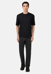 Černé tričko s kulatým výstřihem vyrobené z bavlny, spárované s tmavými kalhotami. Střih je volný, s krátkými rukávy a hladkým povrchem.