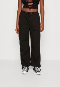 Černé cargo kalhoty s volným střihem, elastickým pasem a šňůrkovým uzávěrem. Spárované s černobílými teniskami.