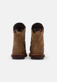 Bruna läderankelboots med en strukturerad yta, en staplad träklack och ett färgglatt randigt foder synligt vid den övre öppningen.