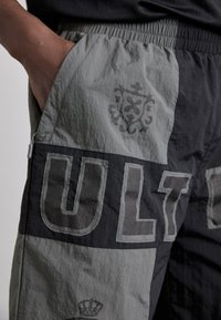 Szürke és fekete, könnyű anyagú cargo rövidnadrág, nagy "ULT" felirattal, diszkrét logóval, rugalmas derékpánttal és oldalsó zsebbel.