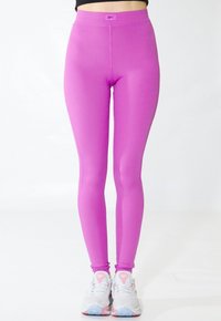 Leggings rosa con acanalado y una cintura alta. Presentan una textura suave y una forma ajustada, combinados con deportivas gris claro.