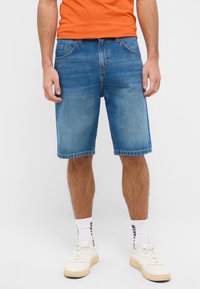 Denimowe szorty w jasnoniebieskim kolorze o prostym kroju, pięć kieszeni, przeszyty brzeg i wyblakły wygląd, połączone z jednolitą pomarańczową koszulą.