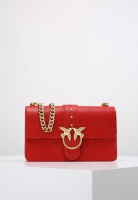 Borsa a tracolla in pelle rossa con motivi in rilievo, hardware dorato, catena e un distintivo motivo di uccello sul blocco.