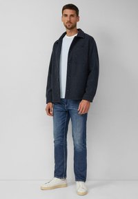 Donkergrijze button-up jacket met een kraag, gedragen over een lichtblauw shirt, gecombineerd met blauwe jeans en witte sneakers. Eenvoudig ontwerp met een zak.