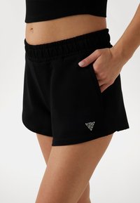 Čierne šortky zo soft materiálu s elastickým pásom, so bočnou vreckom a malým trblietavým trojuholníkovým logom na leme.