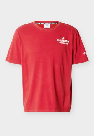 Piros rövid ujjú Champion póló fehér "CHAMPION TRAINING CLUB" felirattal és logóval a mellkason és az ujjon, kerek nyakkivágással és laza szabással.